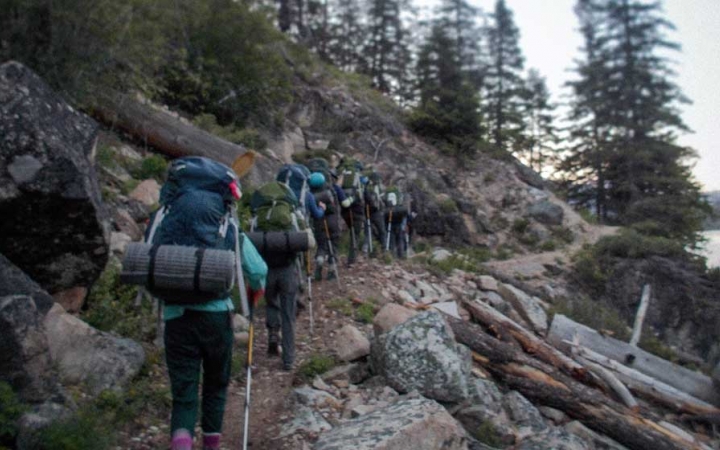 a group of backpackers make their way along a trail beside a body of water